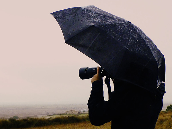 Pau Guerrero amb paraigües, fotografiant el paisatge de Monegros sota la pluja
